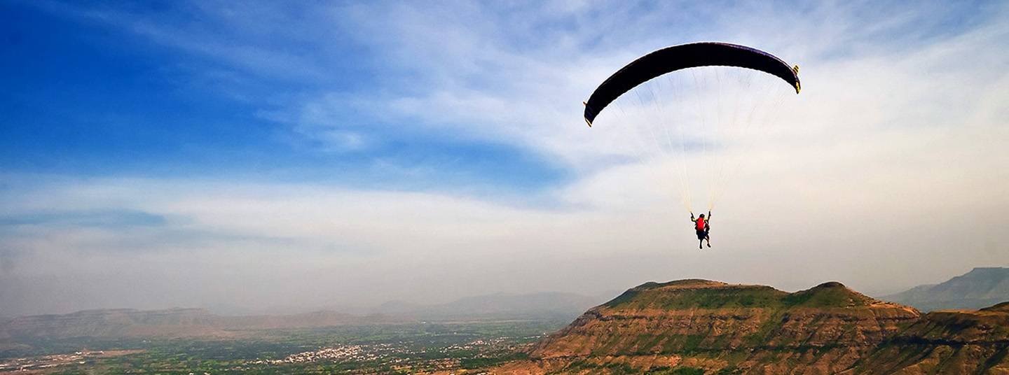 A person parachutes high above a rural landscape.